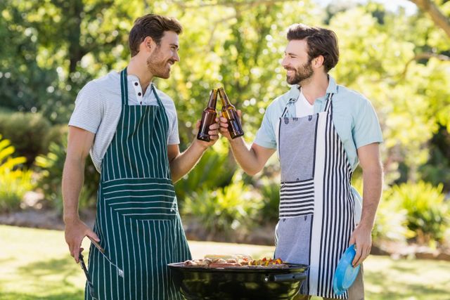 Men toasting beer bottle while preparing barbecue grill in park