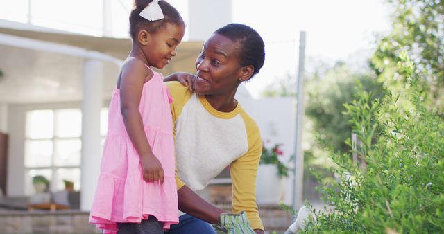 African American mother and young daughter enjoying bonding time while gardening in their backyard. Ideal for content on family activities, outdoor hobbies, lifestyle topics, and childhood education about nature.