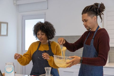 Multicultural couple whisking batter together in bright modern kitchen wearing aprons