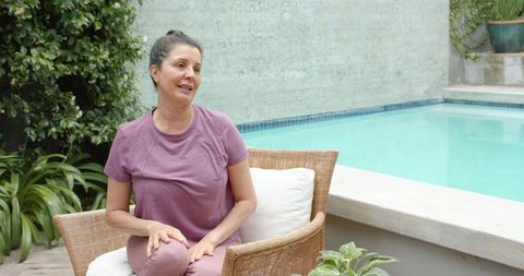 Mature woman sitting and talking on poolside patio wearing mauve outfit