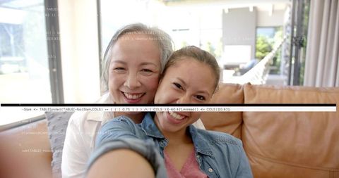 Multigenerational asian mother and daughter taking selfie on couch with code overlay