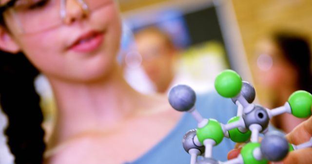A young student examines a molecular model closely, with copy space. The focus on the model suggests a learning environment, a chemistry class.