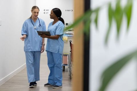 Two nurses walking corridor sharing tablet discussing patient care in hospital radiology