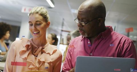 Mature woman and african american senior man collaborating over laptop in open-plan office