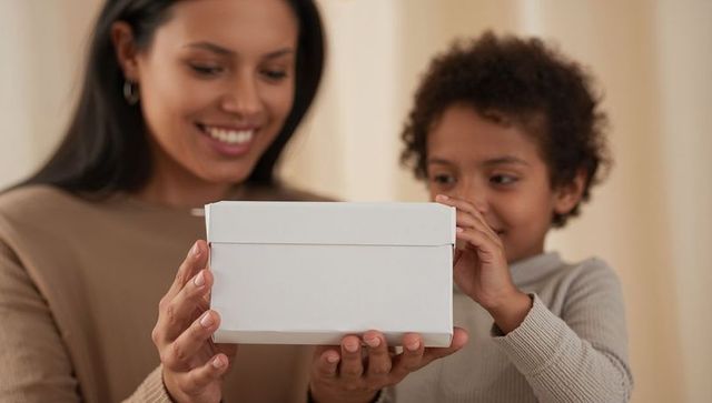 Mother and child sharing white gift box, smiling together in cozy family moment
