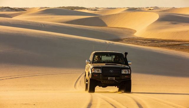 4x4 suv driving across golden sand dunes at sunset, off-road adventure and traction test