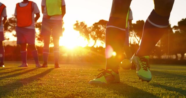 Group of soccer players training on a field during sunset in sports uniforms and gear. The scene emphasizes fitness, teamwork, and youth sports. Ideal for use in sports advertisements, fitness promotions, talent recruitment drives, and youth sports programs.