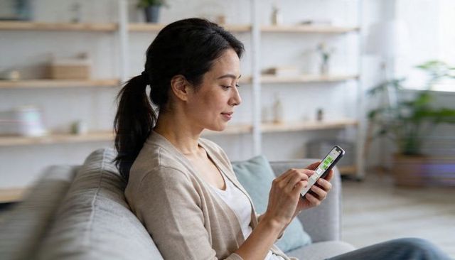 Asian woman relaxing on sofa using smartphone for messaging in modern living room