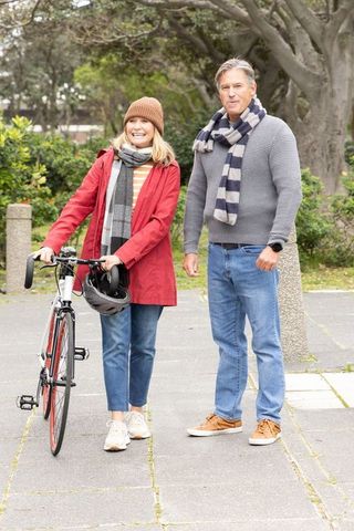 Smiling senior couple posing with bicycle in park during cool-weather stroll