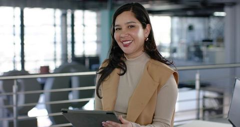 Professional woman smiling while holding tablet on modern office mezzanine