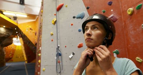 Woman preparing for indoor rock climbing with safety helmet