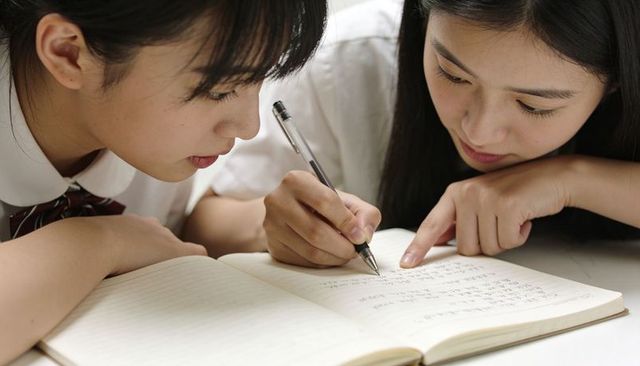 Two asian high school students collaborating, writing asian characters in notebook