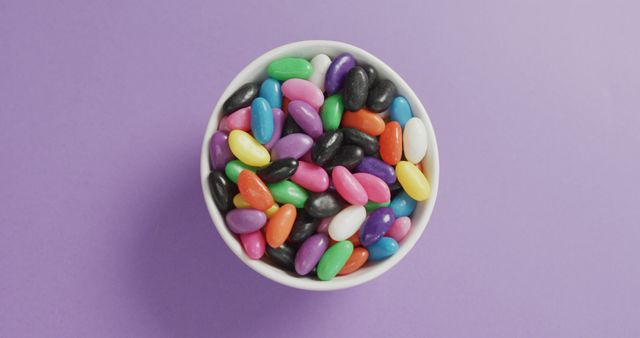 Colorful jelly beans in a white bowl make a vibrant, playful composition against purple background. Ideal for blogs, social media, advertisements, and packaging designs involving sweets and confectionery products.