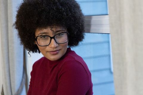 Woman wearing black glasses watching raindrops by window in burgundy turtleneck sweater