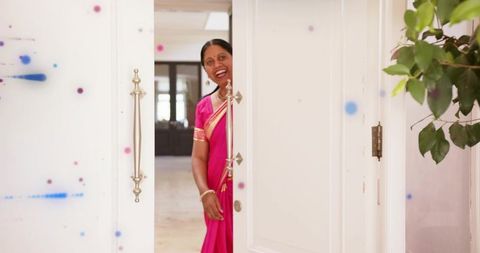Smiling woman peeking through elegant foyer doorway wearing bright pink silk sari