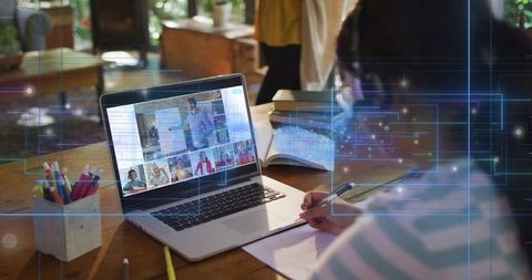 Child writing while attending virtual classroom on laptop at home with notebook and pencils