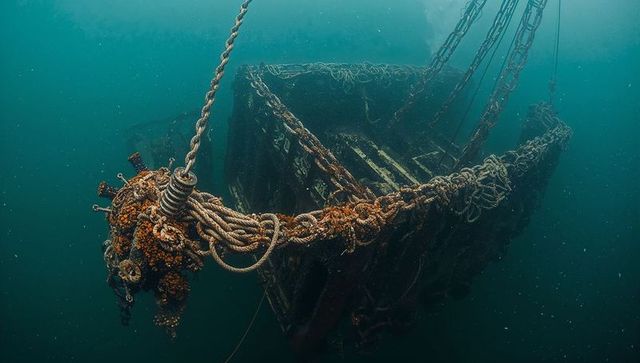 Barnacle-encrusted lifeboat hanging beneath surface with rusted chains and ropes