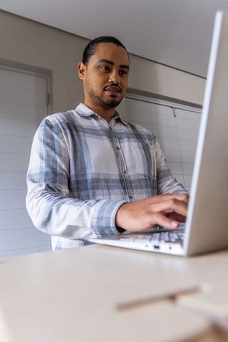 Standing man typing on laptop at home countertop in minimalist modern workspace