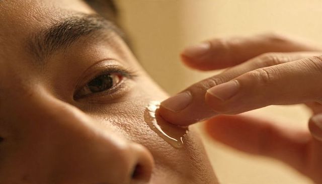 Asian man touching fingertip to clear tear on cheek close-up emotional skincare moment