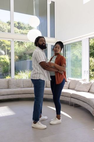 African american couple embracing in modern sunlit living room with large windows