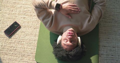 Sunlit man lying on mat listening with headphones, practicing mindfulness and relaxation