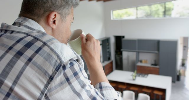 Man sipping coffee in a modern open plan kitchen. Perfect for featuring home lifestyles, morning routines, or interior design showcases.