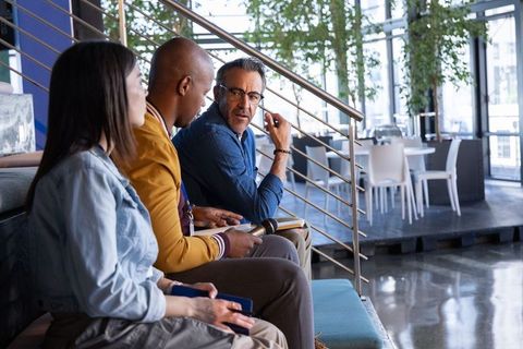 Diverse team discussing ideas in modern office lounge holding microphone and notepad