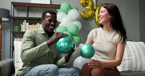 Happy couple preparing birthday party with balloons indoors
