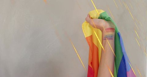 Raised hand holding rainbow pride flag with painted wrist stripes and gold flares