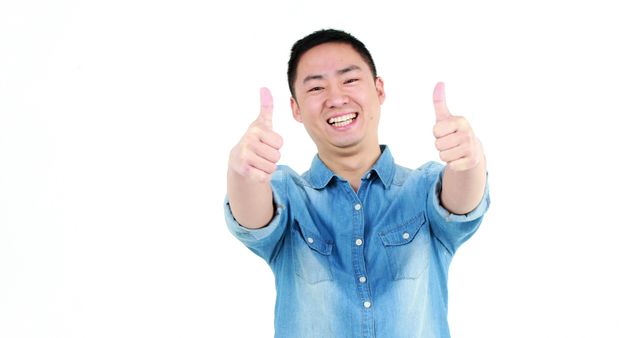 A cheerful young Asian man is giving two thumbs up, with copy space. His bright smile and positive gesture convey a sense of approval or success.