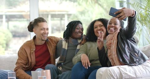 Diverse friends taking selfie on living room couch laughing and sharing cozy moment