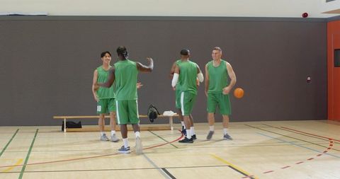 Diverse male basketball team celebrating on indoor court after practice and training