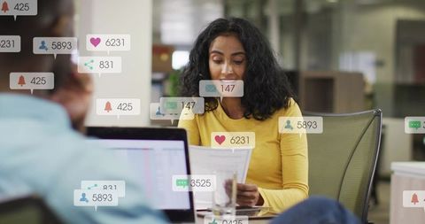 Mid-career Indian woman reviewing documents at office desk with notification overlays