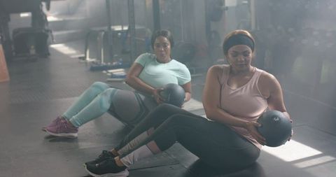 Diverse women performing seated medicine ball twists building core strength in gym