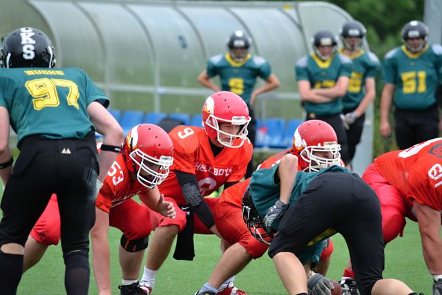 Players converge on a football field wearing red and green uniforms, ready for a play. Ideal for illustrating team sports, youth athletics, coaching strategies, and sports education.