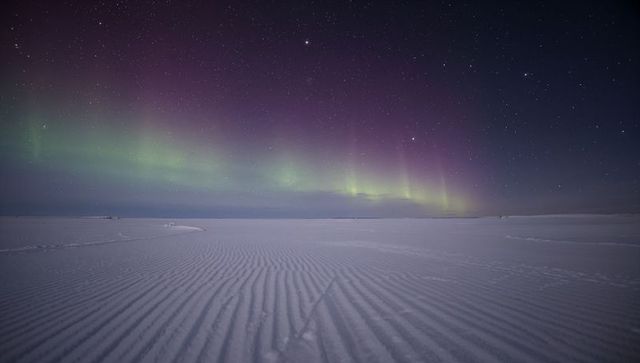 Aurora borealis dancing over rippled arctic snowfield star-filled purple-green night sky
