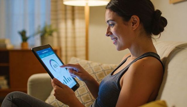Young woman smiling while using tablet dashboard on couch tracking health and fitness app data