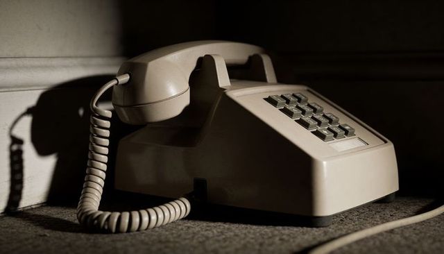 Beige vintage push-button desk phone casting dramatic shadow on carpet