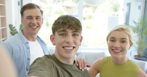 Smiling family taking selfie in sunlit modern living room with teenage son and smartphone