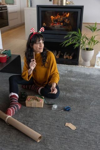 Woman wrapping gifts by fireplace in festive home setting