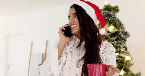 Smiling woman in santa hat enjoys christmas chat by tree