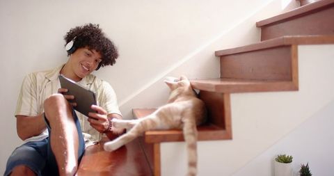 Young man relaxing with tablet and cat on minimalist wood stairs