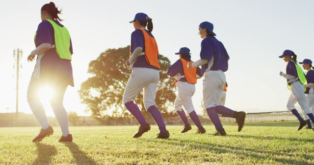 Diverse group of female baseball players exercising on pitch, running and touching the ground. female baseball team, sports training and game tactics.