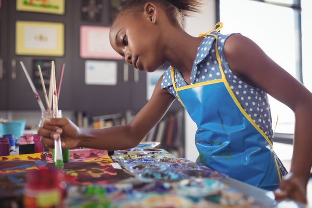 Young girl concentrating on painting in an art classroom. Ideal for educational content, school brochures, art class promotions, and creativity-focused campaigns.
