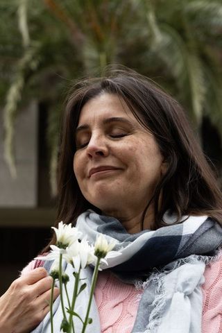 Middle-aged woman holding white daisies, scarf wrapped, eyes closed in serene moment