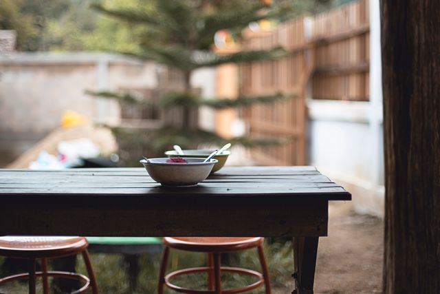Rustic outdoor dining table displays food bowls for a casual meal. Surrounding garden and patio setting create a serene atmosphere. Useful for illustrating outdoor eating, rustic décor, casual gatherings, and tranquil environments.