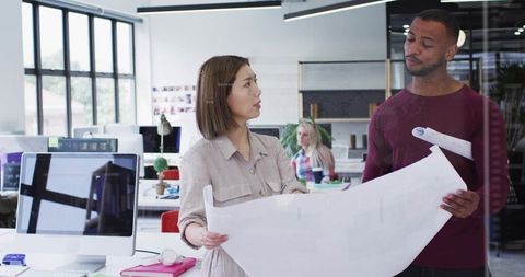 Multicultural Professionals Reviewing Architectural Blueprint in Modern Open-plan Office