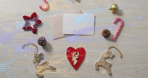 Red heart reindeer ornament on light wood table with envelopes, candy canes, pinecones