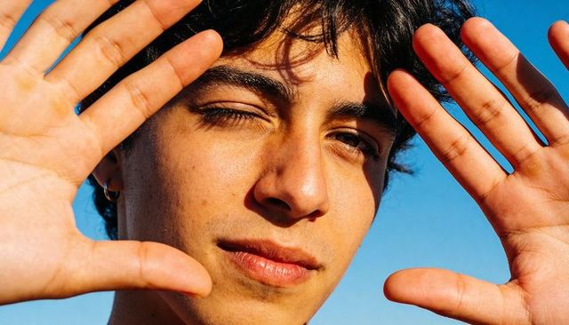Young man squinting and framing with hands under clear blue sky sunlit closeup portrait