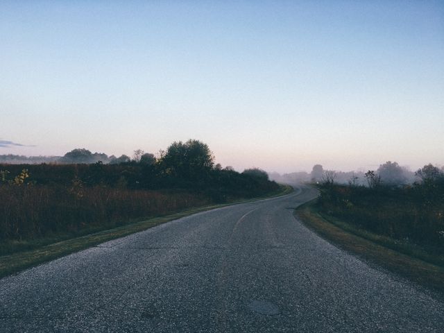 Empty country road winding into misty horizon at dawn with calm, serene atmosphere. Ideal for illustrating concepts of tranquility, peaceful travel, early morning journeys, and scenic rural landscapes. Suitable for backgrounds, contemplative mood settings, travel blogs, and countryside promotions.